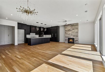 Kitchen with stainless steel microwave, light hardwood / wood-style flooring, a large fireplace, a center island with sink, and tasteful backsplash