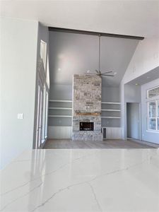 Unfurnished living room with built in shelves, a stone fireplace, vaulted ceiling, and ceiling fan