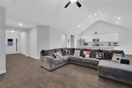 Living room with dark hardwood / wood-style flooring, ceiling fan, and high vaulted ceiling