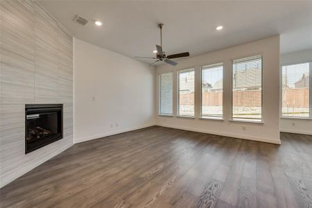 Unfurnished living room featuring a fireplace, a wealth of natural light, ceiling fan, and dark wood-type flooring