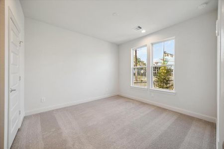 This cozy first-floor bedroom features soft carpeting and large windows that fill the space with natural light. The neutral color palette provides a fresh and inviting feel, while the room offers flexible options for use as a guest bedroom, home office, or personal retreat.