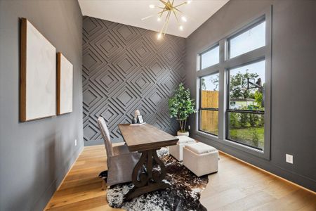 The study features a geometric accent wall, brushed gold chandelier and French doors for privacy.