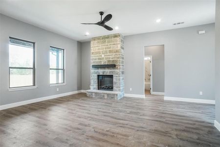 Unfurnished living room featuring a stone fireplace, hardwood / wood-style flooring, and ceiling fan