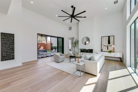 Living room with ceiling fan, light hardwood / wood-style floors, plenty of natural light, and a high ceiling