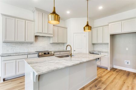 Kitchen with hanging light fixtures, an island with sink, backsplash, and high end stove