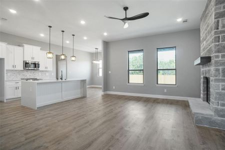 Kitchen featuring light hardwood / wood-style floors, a stone fireplace, an island with sink, and ceiling fan