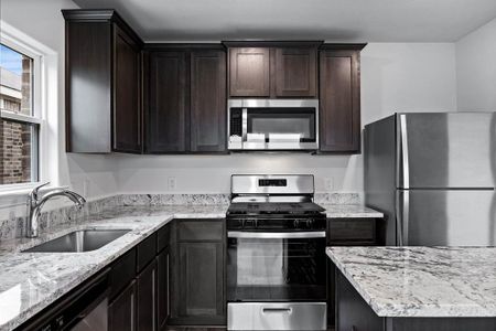 Kitchen featuring dark brown cabinetry, stainless steel appliances, light stone counters, and sink