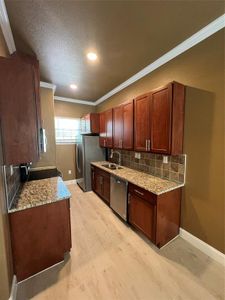 Kitchen with stove, light stone countertops, decorative backsplash, and stainless steel dishwasher