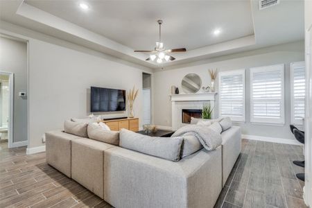 Living room with light hardwood / wood-style floors, ceiling fan, and a raised ceiling