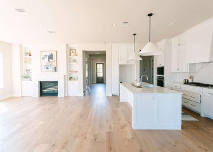 Kitchen featuring a high end fireplace, light hardwood / wood-style flooring, white cabinetry, an island with sink, and pendant lighting