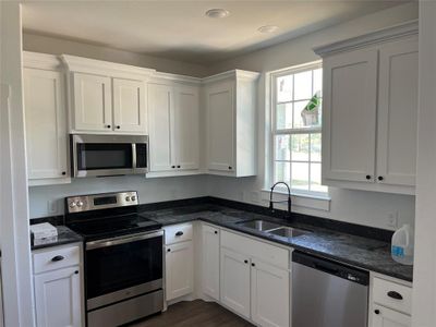 Kitchen featuring dark stone countertops, sink, stainless steel appliances, and white cabinets