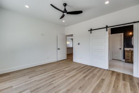 Master bedroom featuring connected bathroom, a barn door, a remote operated ceiling fan