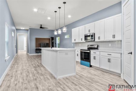 Kitchen with appliances with stainless steel finishes, pendant lighting, a kitchen island with sink, and white cabinetry