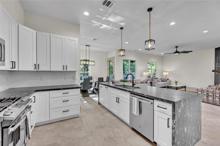 A modern kitchen with white cabinets, stainless steel appliances, granite countertop island and pendant lights