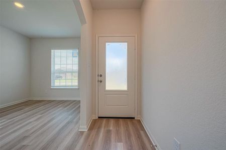 A room with laminate flooring, a window with blinds, a closed door with a decorative glass panel.