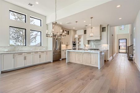 Kitchen with a high ceiling, pendant lighting, an island with sink, and light hardwood / wood-style flooring