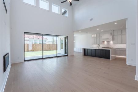 Unfurnished living room featuring sink, a high ceiling, light hardwood / wood-style flooring, and ceiling fan