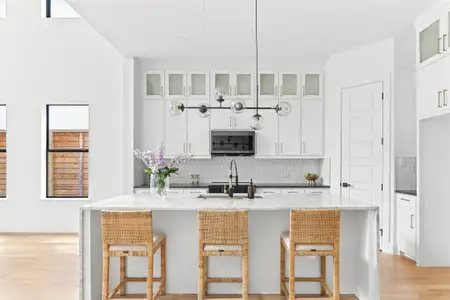 Kitchen featuring light stone countertops, light hardwood / wood-style flooring, a kitchen island with sink, hanging light fixtures, and white cabinetry