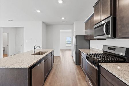 Kitchen with light wood-type flooring, sink, a kitchen island with sink, stainless steel appliances, and light stone countertops