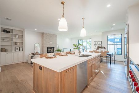 Kitchen featuring an island with sink, sink, appliances with stainless steel finishes, a fireplace, and light hardwood / wood-style floors