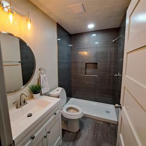 Bathroom with a textured ceiling, hardwood / wood-style floors, toilet, tiled shower, and vanity