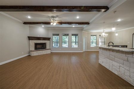 Unfurnished living room featuring ornamental molding, beamed ceiling, a fireplace, and dark wood-type flooring