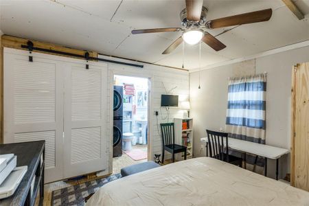 Bedroom featuring a barn door, connected bathroom, a closet, stacked washer and dryer, and ceiling fan