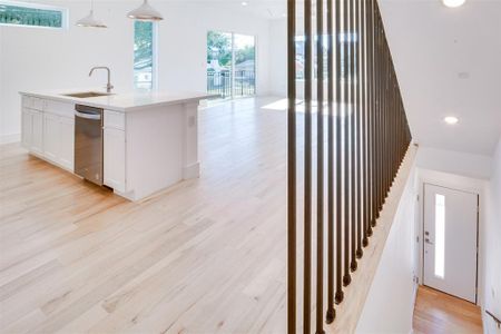 Kitchen with dishwasher, hanging light fixtures, sink, white cabinets, and light hardwood / wood-style floors