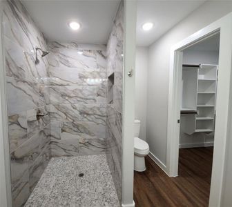 Bathroom featuring tiled shower, toilet, and wood-type flooring