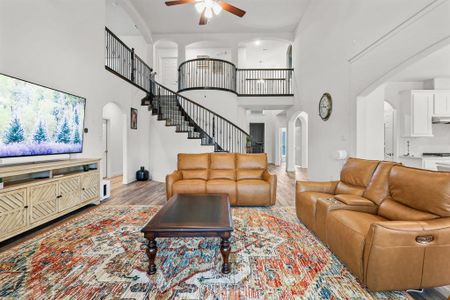 Living room with ceiling fan, light wood-type flooring, and a high ceiling