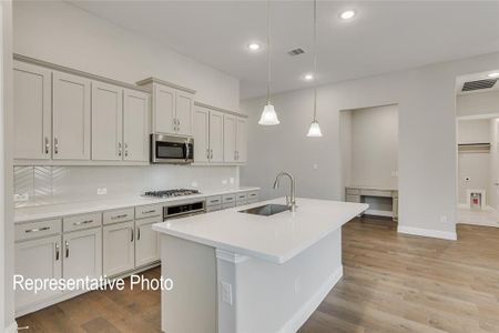 Kitchen featuring backsplash, sink, decorative light fixtures, light hardwood / wood-style floors, and a kitchen island with sink