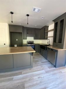 Kitchen featuring light wood-type flooring, stainless steel electric range, dishwashing machine, sink, and hanging light fixtures