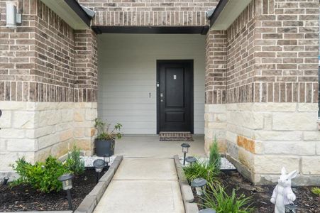 The entrance features a covered porch accented by a two-tone brick facade, complemented by stone detailing. A welcoming black front door is framed by well-maintained landscaping, adding to the home's curb appeal.
