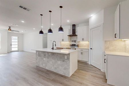 Kitchen with an island with sink, hanging light fixtures, wall chimney range hood, white cabinetry, and stainless steel range with electric cooktop