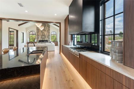 Kitchen featuring wall chimney exhaust hood, light hardwood / wood-style flooring, lofted ceiling, and dark stone countertops