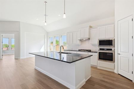 Kitchen with decorative backsplash, white cabinetry, appliances with stainless steel finishes, light hardwood / wood-style floors, and extractor fan