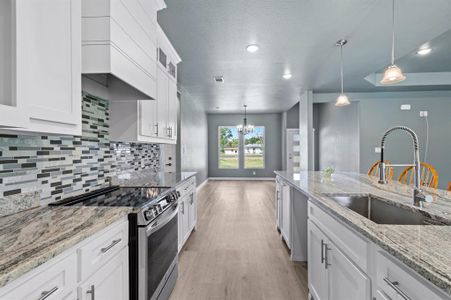 Kitchen featuring electric stove, sink, hanging light fixtures, white cabinets, and light hardwood / wood-style floors