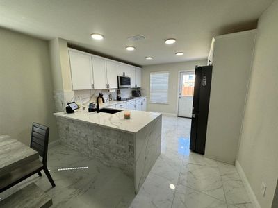 Kitchen featuring kitchen peninsula, tasteful backsplash, light stone countertops, black refrigerator, and sink