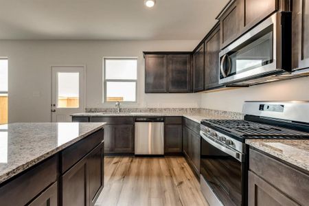 Kitchen featuring stainless steel appliances, sink, light stone counters, dark brown cabinetry, and light hardwood / wood-style flooring