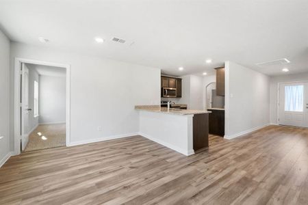 Kitchen featuring appliances with stainless steel finishes, light hardwood / wood-style floors, kitchen peninsula, sink, and light stone counters