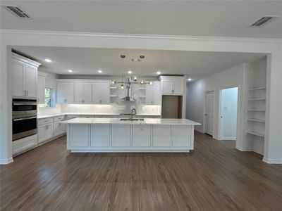 Kitchen with wood-type flooring, a center island, wall chimney exhaust hood, pendant lighting, and white cabinets