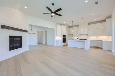 Kitchen with ceiling fan with notable chandelier, white cabinetry, a kitchen island with sink, and a stone fireplace