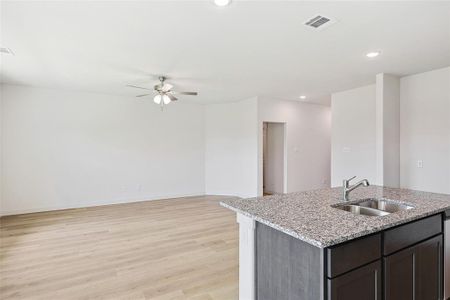 Kitchen featuring ceiling fan, dark brown cabinetry, an island with sink, sink, and light wood-type flooring