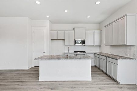 Kitchen with light hardwood / wood-style flooring, light stone counters, a kitchen island with sink, sink, and gray cabinetry