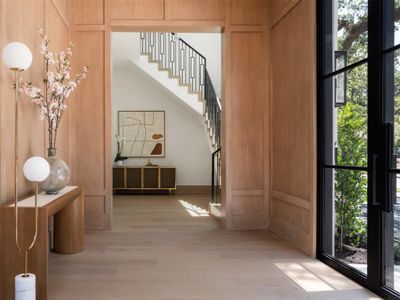 The privatized foyer opens to a soaring 23-foot tall room where the custom staircase takes center stage, accompanied by the majestic presence of a century oak tree out front.