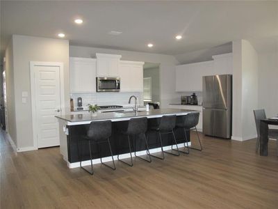 Kitchen with stainless steel appliances, a breakfast bar, dark hardwood / wood-style flooring, white cabinetry, and a center island with sink