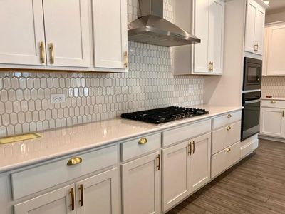 Kitchen featuring white cabinetry, wall chimney range hood, black appliances, dark hardwood / wood-style floors, and tasteful backsplash