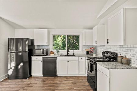 Kitchen with sink, black appliances, white cabinetry, and light stone counters