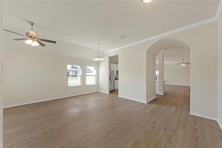 Spare room featuring light wood-type flooring, ceiling fan with notable chandelier, and crown molding