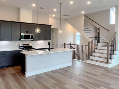 Modern kitchen with sleek charcoal cabinetry, pristine white countertops, and designer pendant lighting, seamlessly flowing into an open living space.